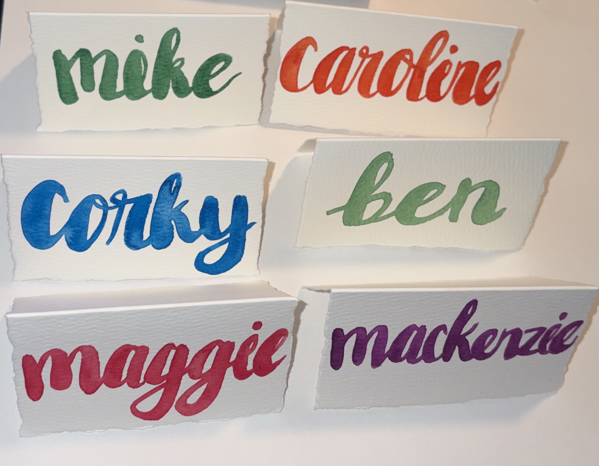 Hand-lettered watercolor place cards with names in bright, bold colors