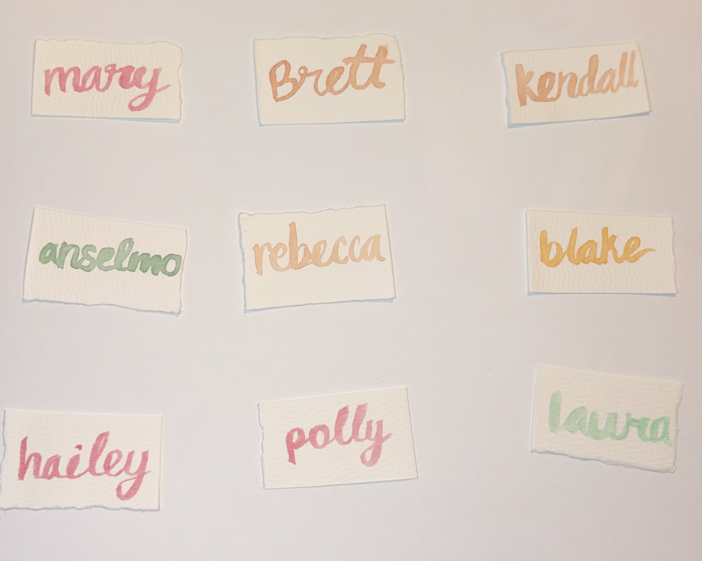 Hand-lettered watercolor place cards with names in soft pastel tones